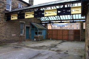 This area was the terminus for the railway. Weighing office on the left behind which was the upholsterer's shop, above the upholsterer's was the male clothing shop, behind the camera both upstairs and down was the bakehouse. On the right under the glass roof is the back door to the general stores. The black and yellow beams are part of the gantry used to hoist supplies from the train. It is believed that the rails of the old railway line are still in situ covered by asphalt.